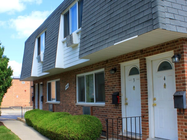 Two story apartment building with red brick, black roofing tile and white trim.