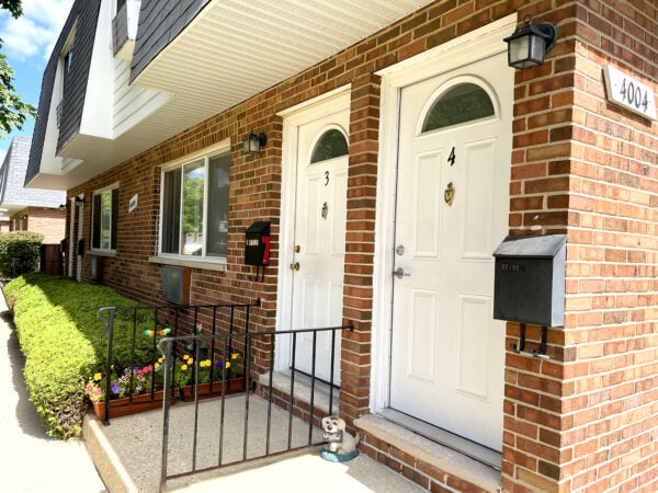 Two white doors on a red brick apartment building. Red, yellow and orange flowers line the entrance step to one of the doors.