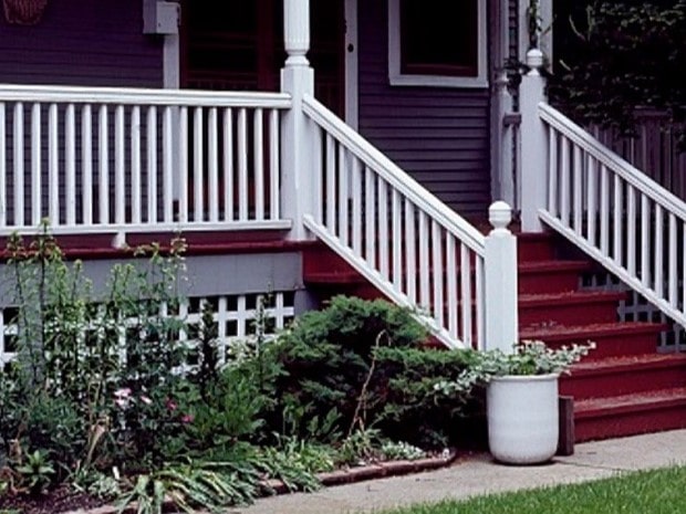 Front steps and porch of a house with white railings, red steps, and plants.