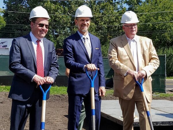 Three men smiling with hard hats and shovels
