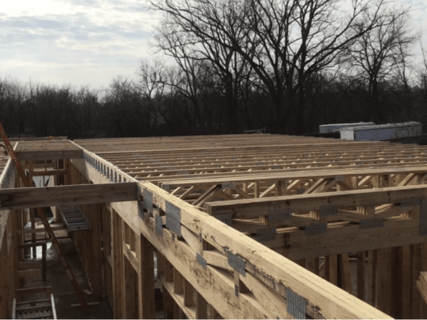 Construction site of wooden trusses. Bare trees in the background.