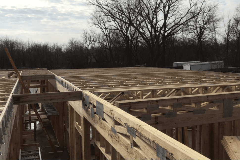 Construction site of wooden trusses. Bare trees in the background.