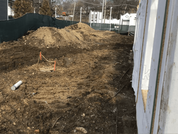 Construction site with dirt and a sewer grate surrounded by construction fencing.