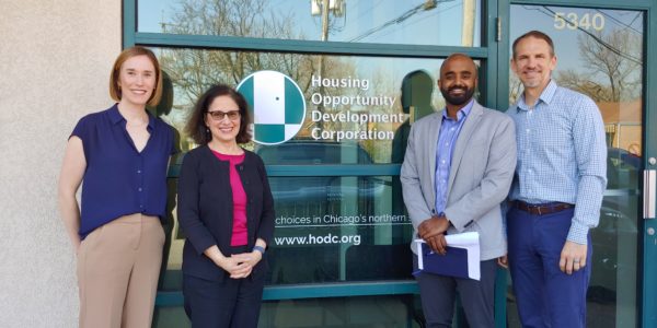 Two women and two men pose in front of the front entrance of a building with the HODC logo on the window behind them.