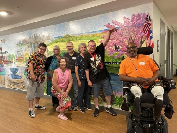 People posing in front of a mural of a landscape painted on a wall.