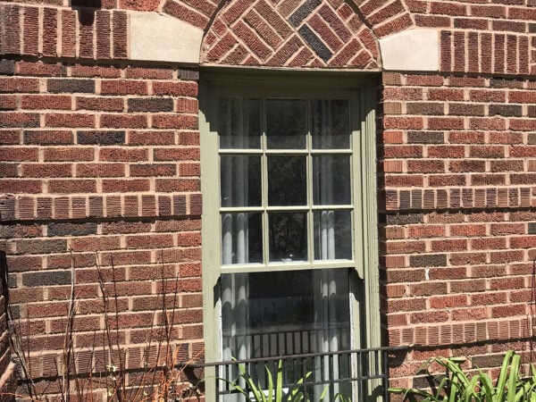 Window of building surrounded by red brick and green plants in front of the building.