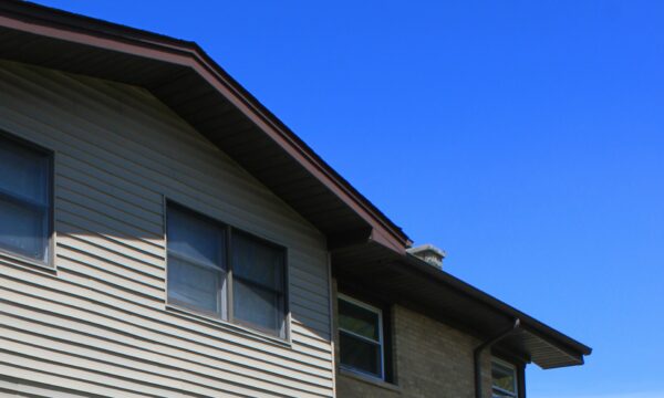 Building with light tan siding and light tan brick. Brown trim on the windows and a blue sky above.