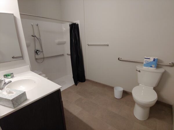 A bathroom with a roll-in shower, white toilet and white sink.