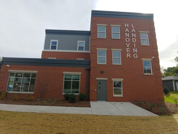 Three story apartment building with red brick and light blue-grey siding.
