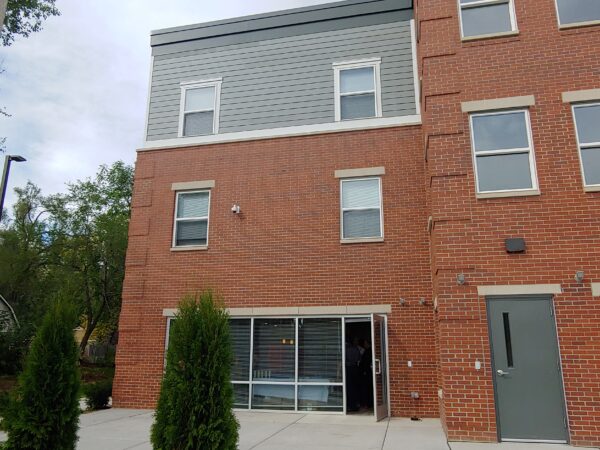 Three story apartment building with red brick and light blue-grey siding.