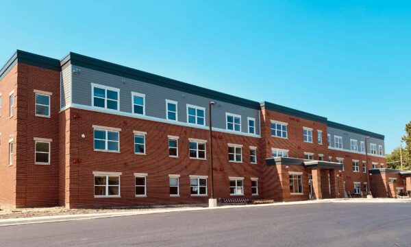 Three story apartment building with red brick, grey siding and white window trim.