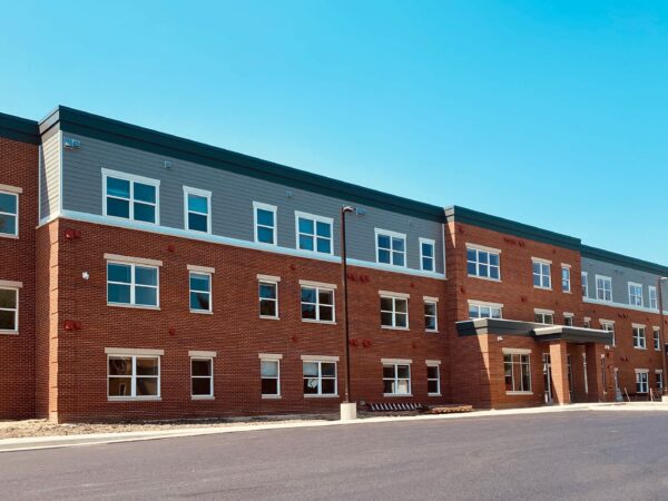 Three story apartment building with red brick, grey siding and white window trim.