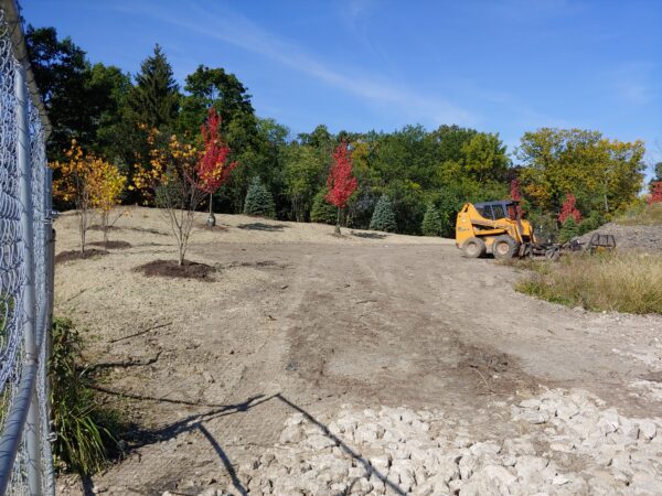 Rocky construction site with small trees with fall colored leaves and a yellow construction vehicle.