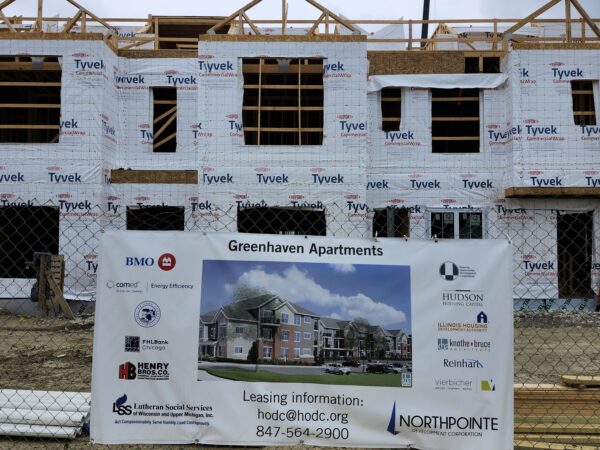 A three story building under construction with a large sign that shows a redering of what the building would look like.