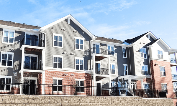 Three-story apartment building with red brick, grey siding and white trim.