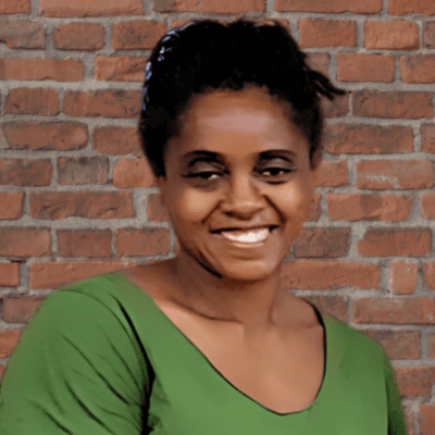 Black woman wearing a green shirt smiles in front of a brick wall.