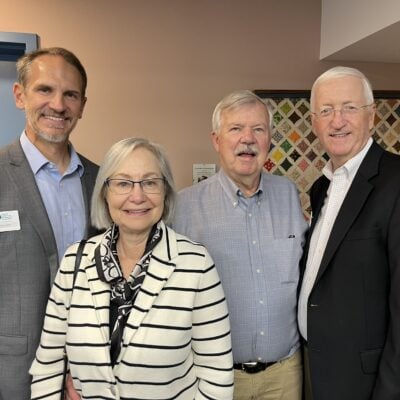 Three men and a woman pose together. The mood is celebratory and friendy.