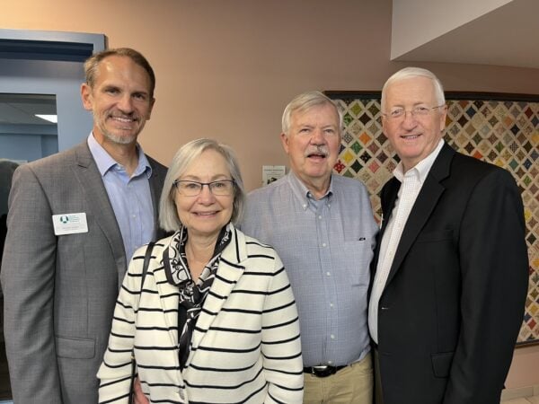 Three men and a woman pose together. The mood is celebratory and friendy.
