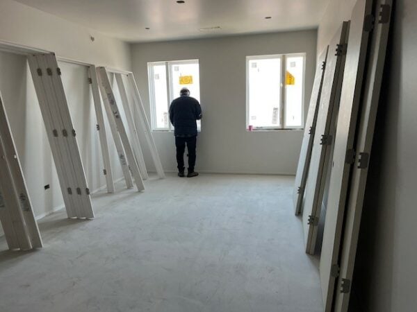 The interior of a construction site, a man looks out a window. Doors lean against the wall.