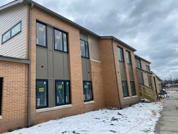 A two-story apartment building with light-brown bricks and windows. Snow on the ground outside the building.