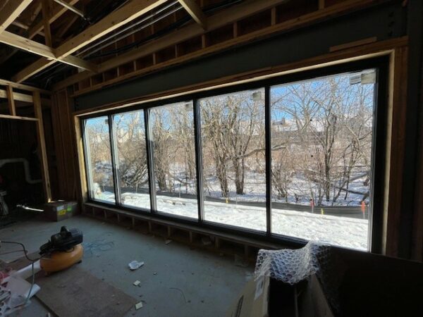 A row of large windows in a room that is under construction shows a winterscape of trees.