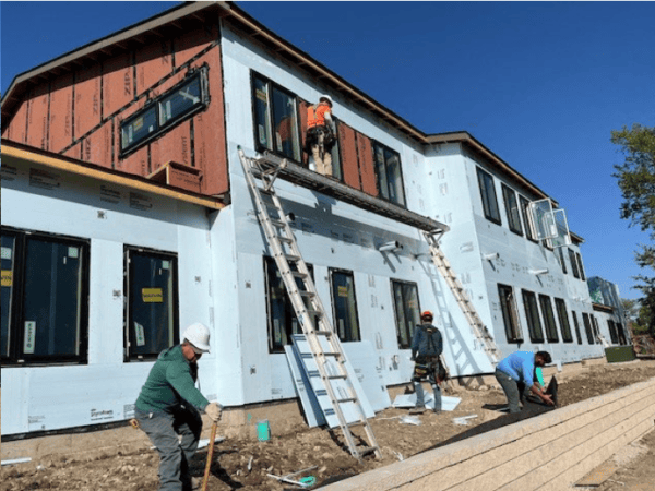 Men work on ladders to stall windows and siding on a two-story apartment building under construction.