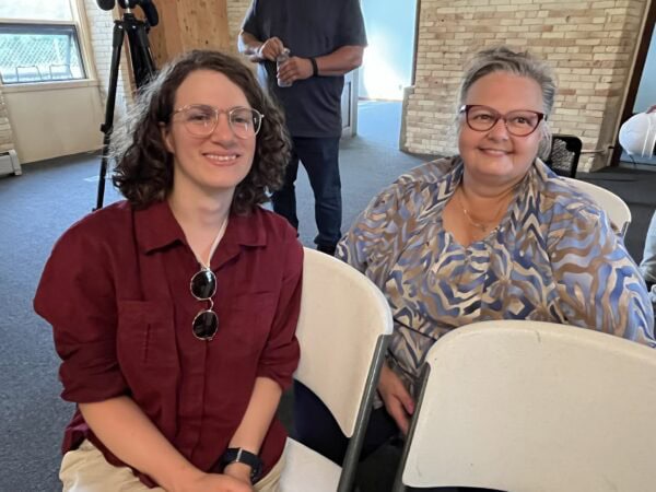 A younger white woman with dark shoulder-length hair sits next to an older white woman with grey hair in a bun.