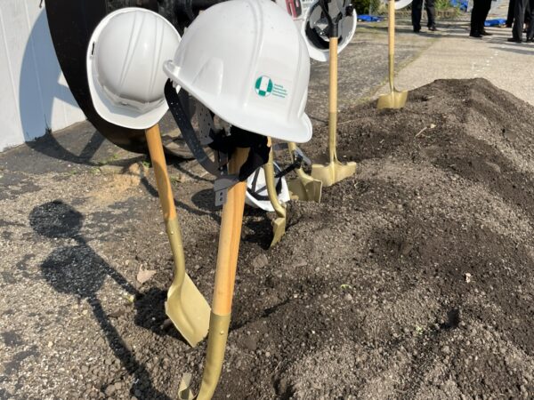 White helmets with the HODC logo are perched on the handles of golden shovels standing up in a pile of dirt.