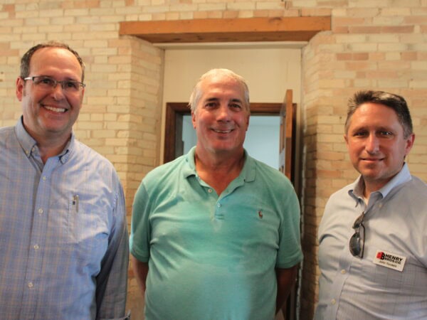 Three white men pose together. Light brick and wood background.