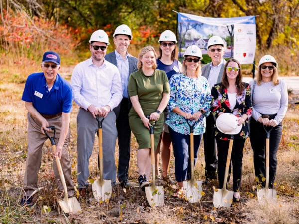 People wearing white hard hats pose with shovels.