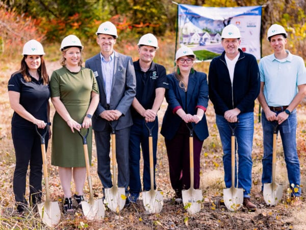 People wearing white hard hats pose with shovels.