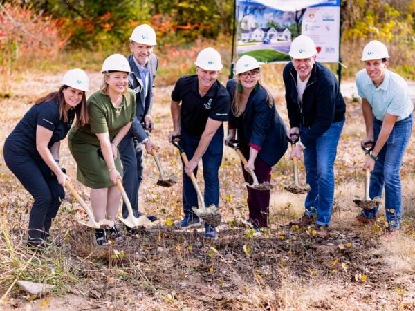 People wearing white hard hats pose with shovels as if they are digging in the dirt.