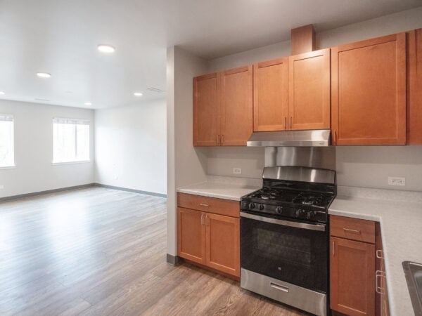 Looking out from the kitchen with oak cabinets, bright light streams through the windows of an apartment living room.