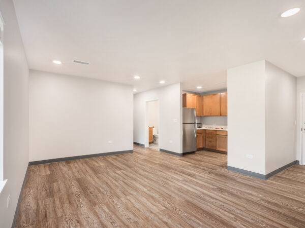 Interior of an empty apartment with white walls, a small kitchen with a refrigerator and oak cabinets.