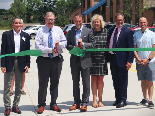 Professionally dressed men and women cut a large green ribbon in front of a two story apartment building.
