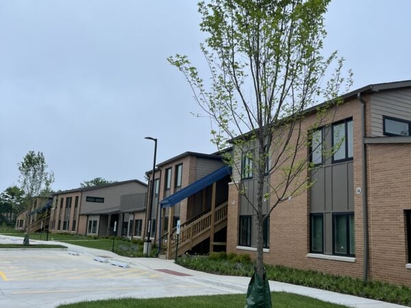 Trees in front of a two story apartment building with green grass.