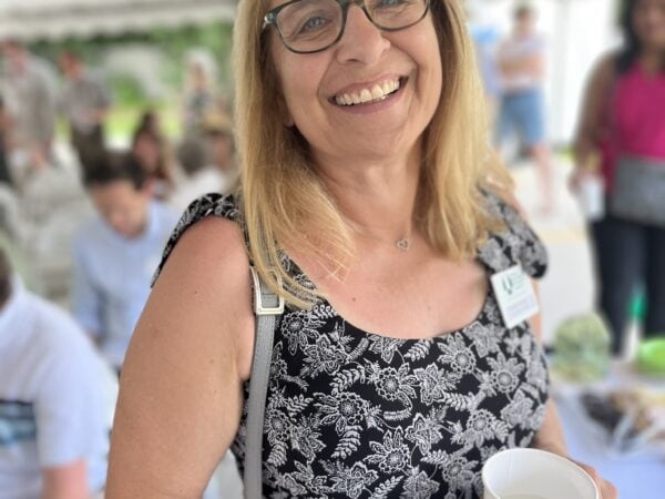 A woman poses under a tent with people behind her. The mood is warm and upbeat.