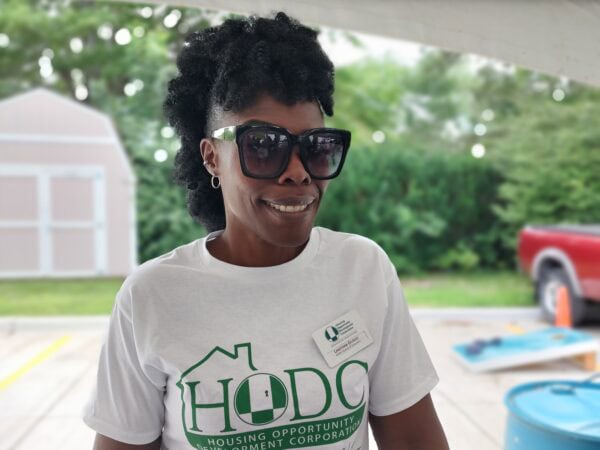 A black woman wearing a tshirt with an HODC logo on it poses under a tent during an outdoor event.