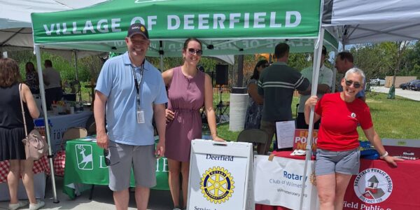 People posing under a green tent with the words Village of Deerfield.