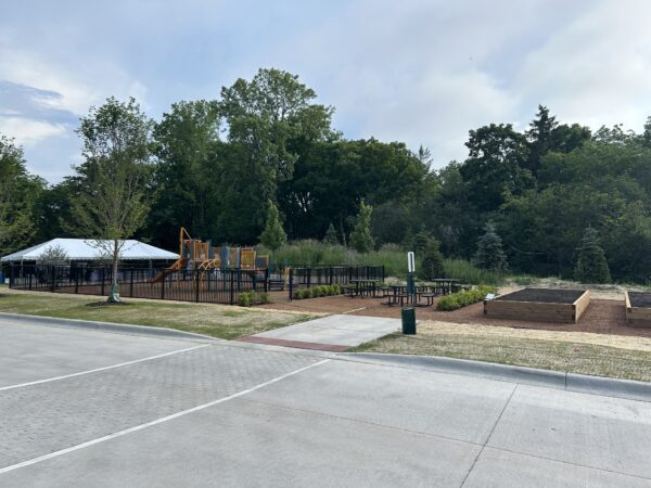 A playground and community garden are across a parking lot. A white tent is visible in the background.