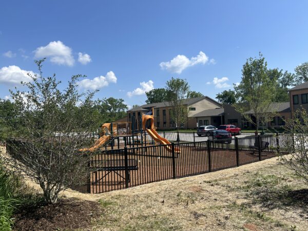 A playground behind a black fence with a two story apartment building in the background.
