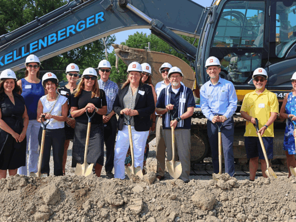 A group of people wearing hard hats and holding shovels stand in front of a bulldozer at a construction site.