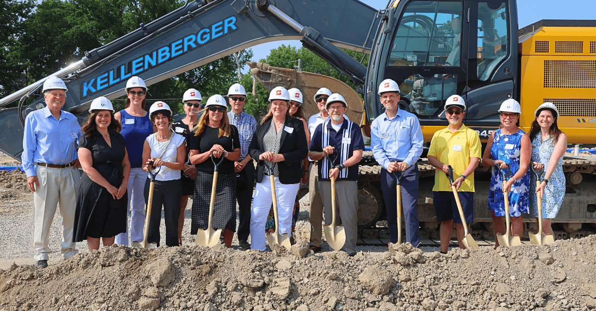 A group of people wearing hard hats and holding shovels stand in front of a bulldozer at a construction site.