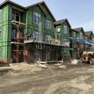 A three story apartment building is under construction with scaffolding and building equipment.