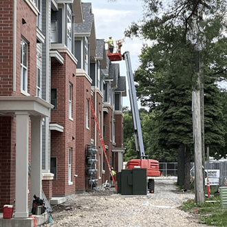 Apartment building under construction with red brick. Workers on a crane are working on the building.
