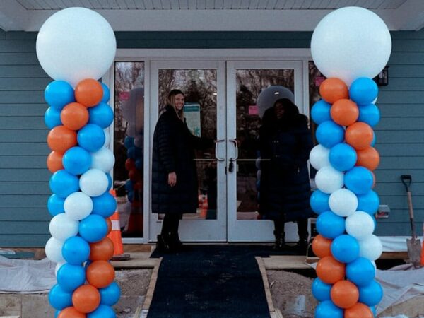 A newly built house is decorated for an event. The entrance features balloon columns in white, blue, and orange, with a snowy path leading inside.
