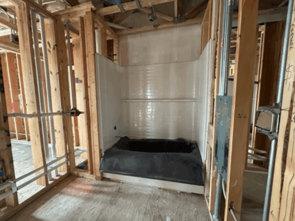 Construction site showing the walls of a shower with exposed studs on either side.