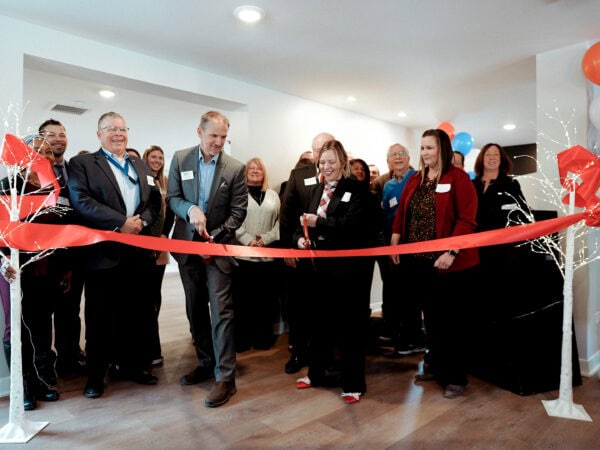Professionally dressed people prepare to cut a wide red ribbon with oversized scissors.