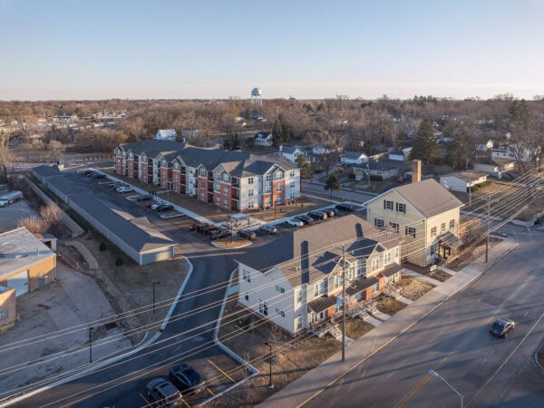 Aerial view of a contemporary apartment complex with parking and nearby houses in a suburban area.