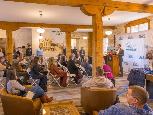 Taylor Place grand opening speaking program with attendees listening to a speaker at a podium.